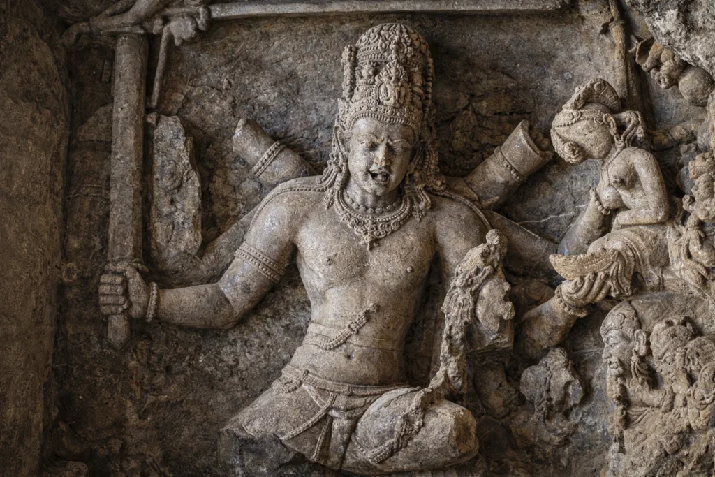 Ancient stone relief carving of a multi-armed deity holding a demon aloft.